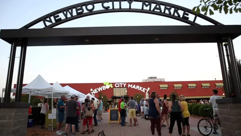 Exterior view of NewBo City Market with its red building, green trees, and a clear blue sky