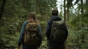 Two hikers with backpacks walking through a lush green forest