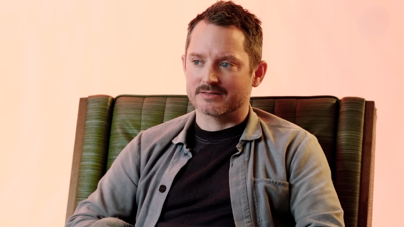 Elijah Wood sitting in a chair during an interview, reflecting on his life story in Iowa