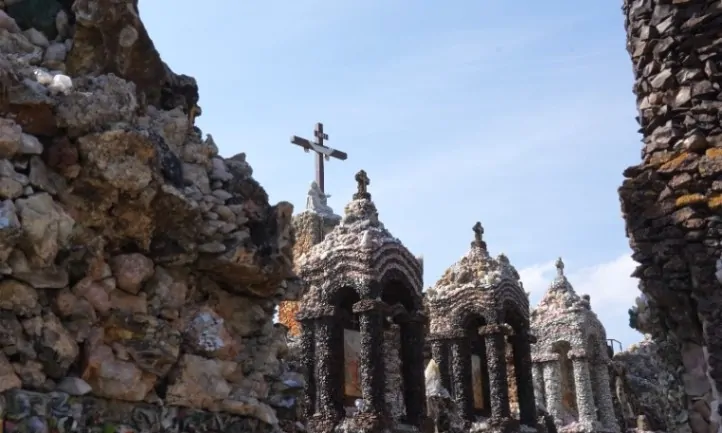 A stone building with detailed arches and columns is seen from below, crowned by a cross