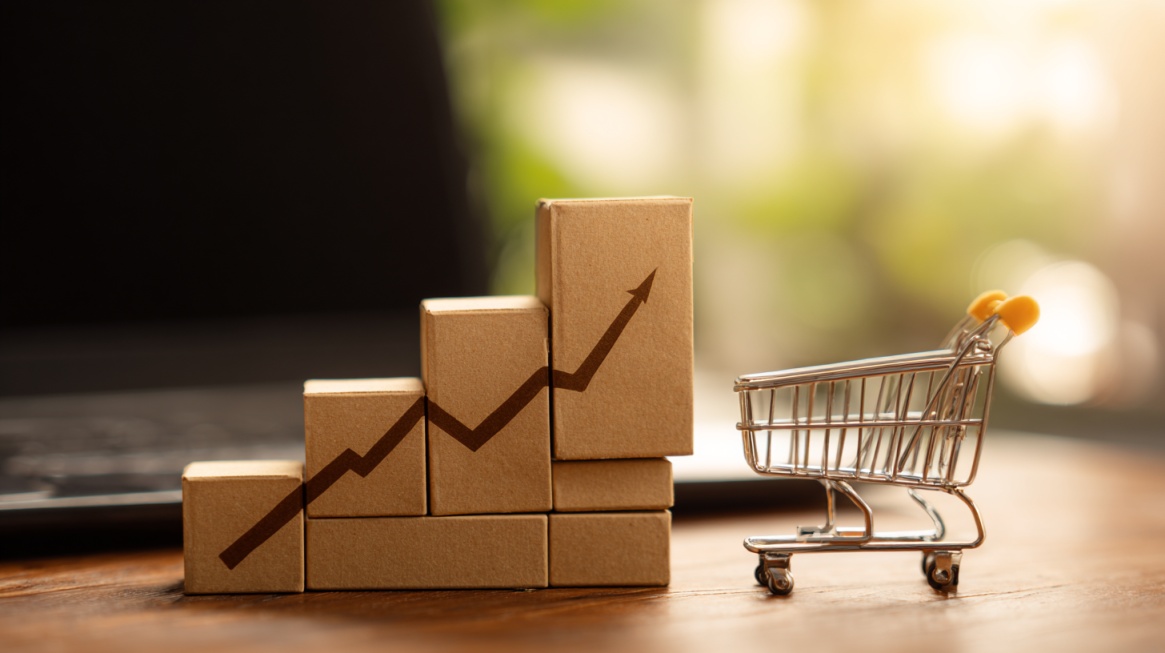 Stacked boxes with an upward growth arrow beside a miniature shopping cart, symbolizing rising ecommerce sales