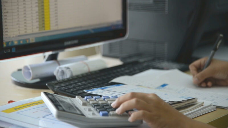 Worker calculates wage figures beside a computer and paperwork