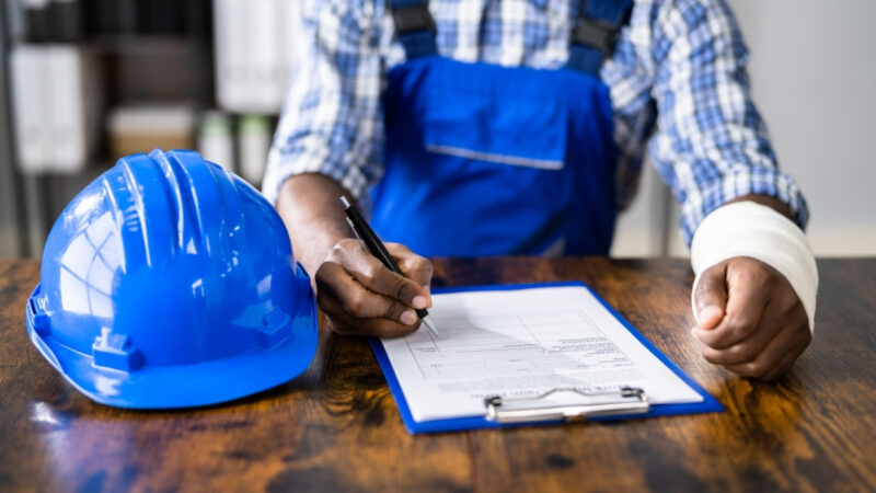 Injured construction worker fills out a workers’ compensation form beside a hard hat
