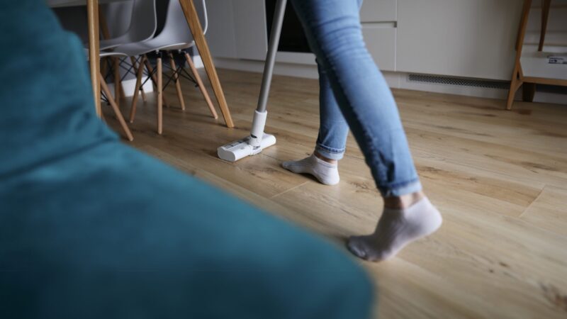 A person vacuums a wooden floor inside a home