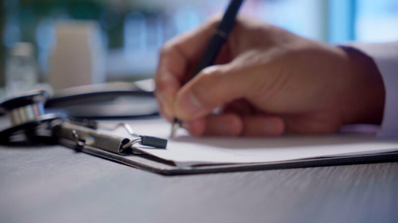 Doctor writes on a clipboard beside a stethoscope