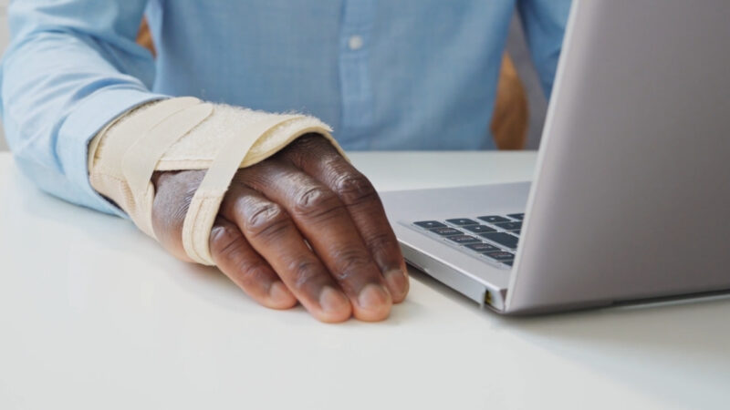 Injured worker with a bandaged wrist sits beside a laptop