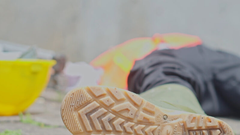 Injured construction worker on the ground beside a yellow hard hat